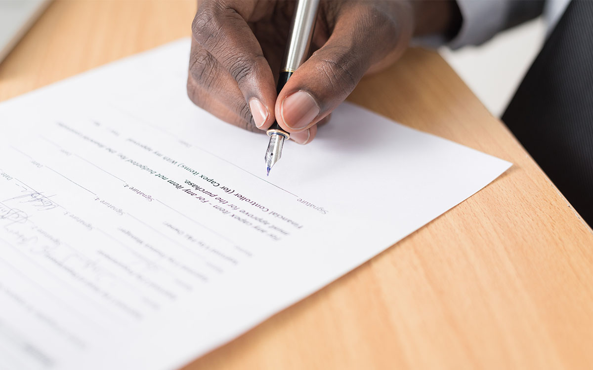 A person’s hand about to sign a document with a pen