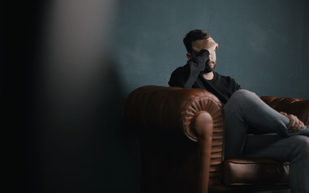 A man holds his head while sitting on a sofa