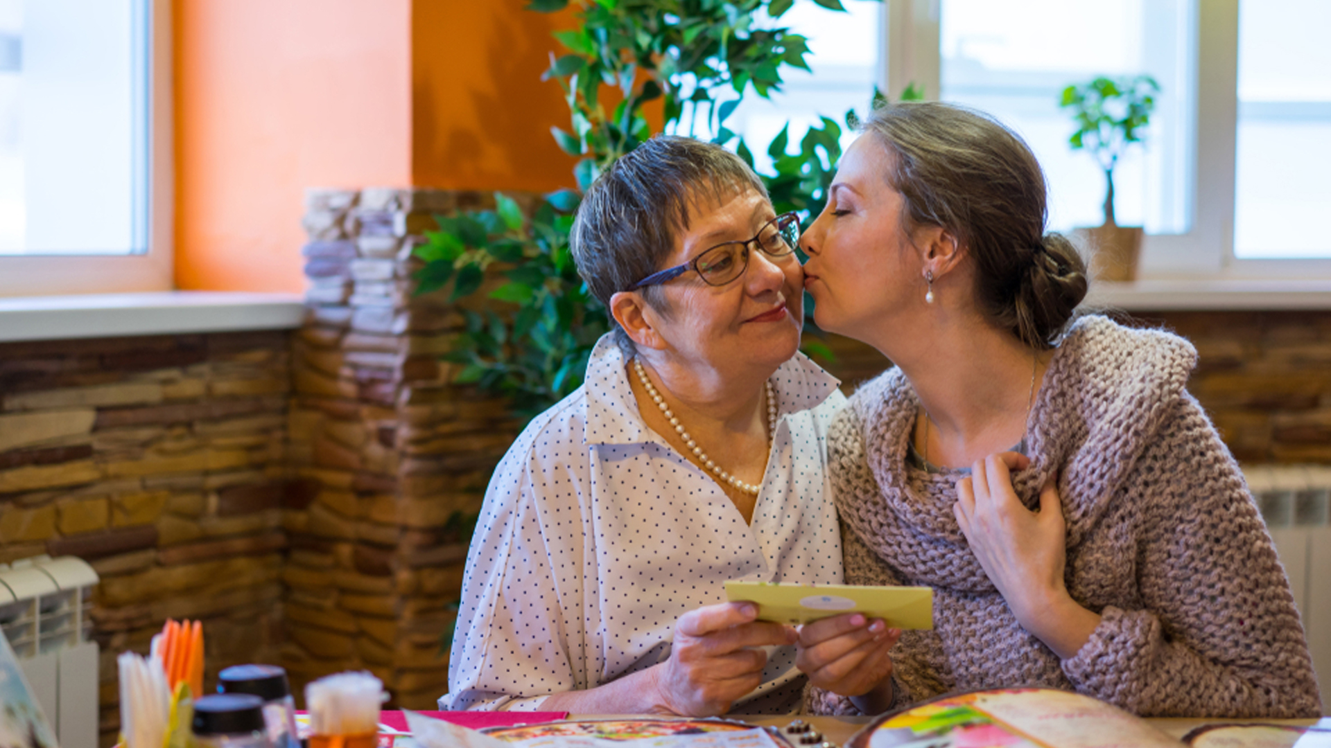 A woman gives another woman a kiss on the cheek.